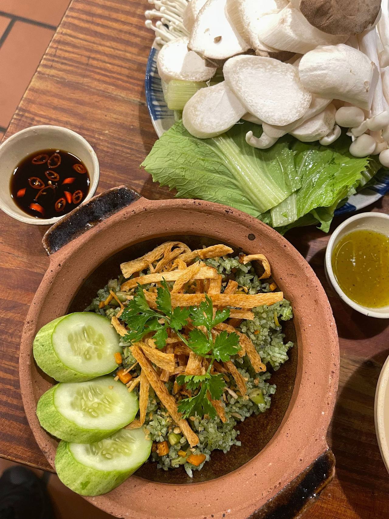 Cơm xanh trong nồi đất rắc đậu hũ ky chiên giòn, dưa leo cắt khoanh và rau mùi, bên cạnh đĩa nấm và chén nước chấm