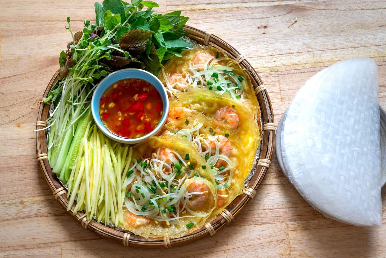 Bánh xèo vàng nghệ nhân tôm, giá, kèm xoài bào sợi, rau thơm, chén nước mắm ớt và miếng bánh tráng, trên mẹt tre