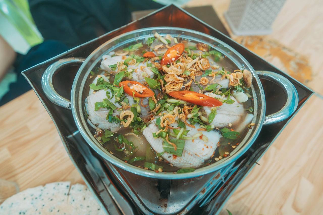 Nồi lẩu cá nhìn từ trên với ớt tươi, hành phi và rau thơm trên bếp mini, bánh tráng đặt bên cạnh