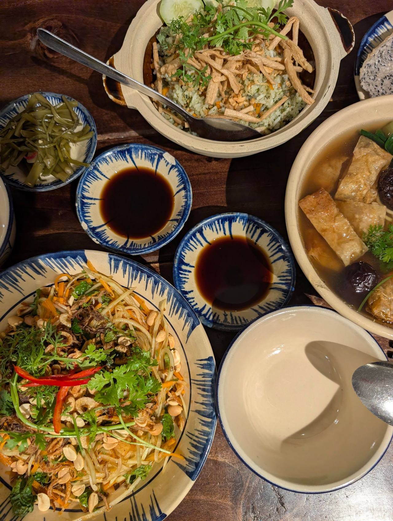 Mâm các món rau đậu nhìn từ trên: gỏi rau, canh đậu hũ, nồi đất, chén nước tương và đĩa dưa muối trên bàn gỗ